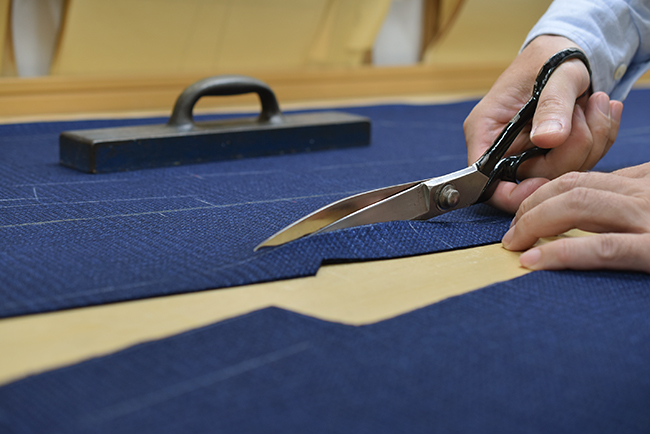 裁断台で前身頃をカットする手元の写真。カシミヤ混の柔らかさが伝わる。